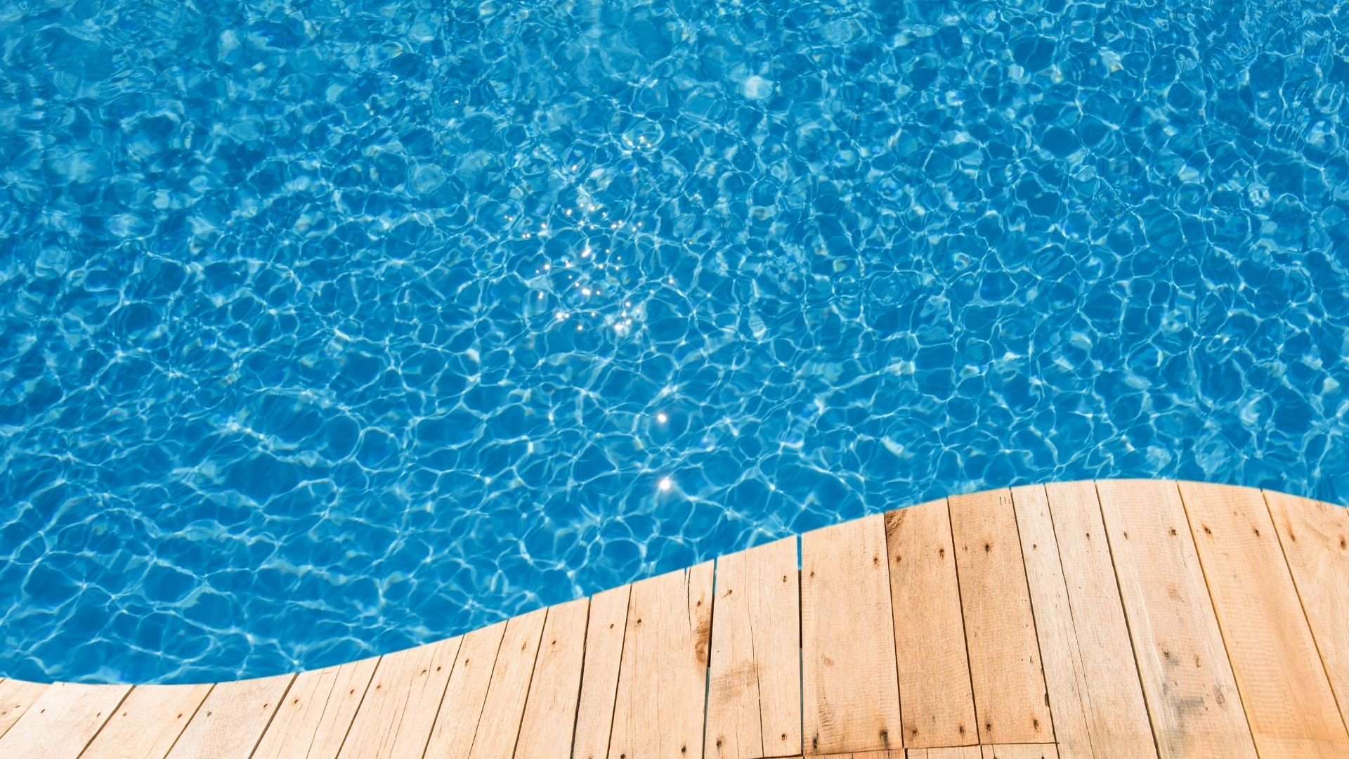 Clear blue pool water with ripples and wooden deck edge beside it