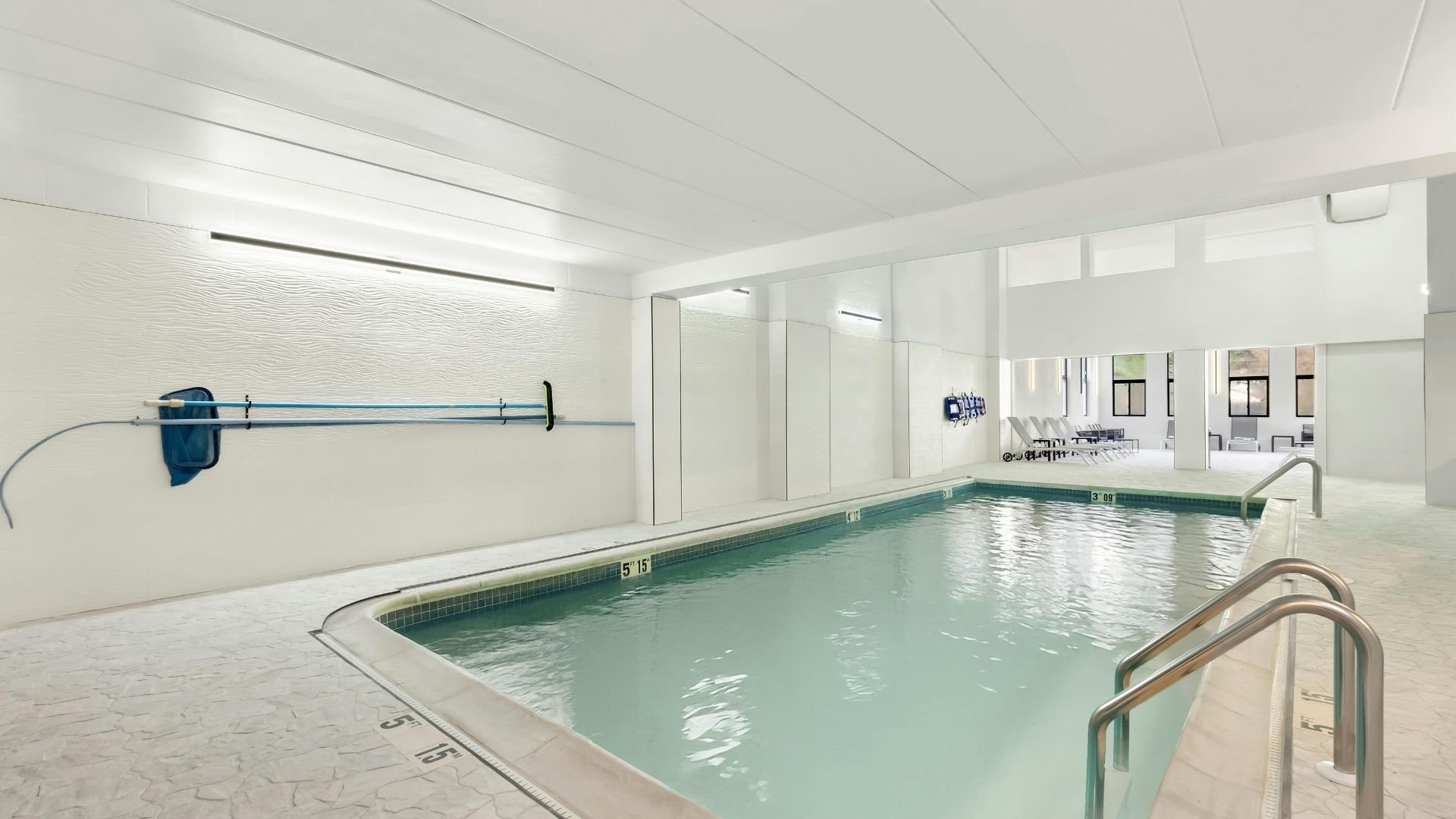 Modern indoor swimming pool with clear water, handrails, and pool maintenance equipment on wall.
