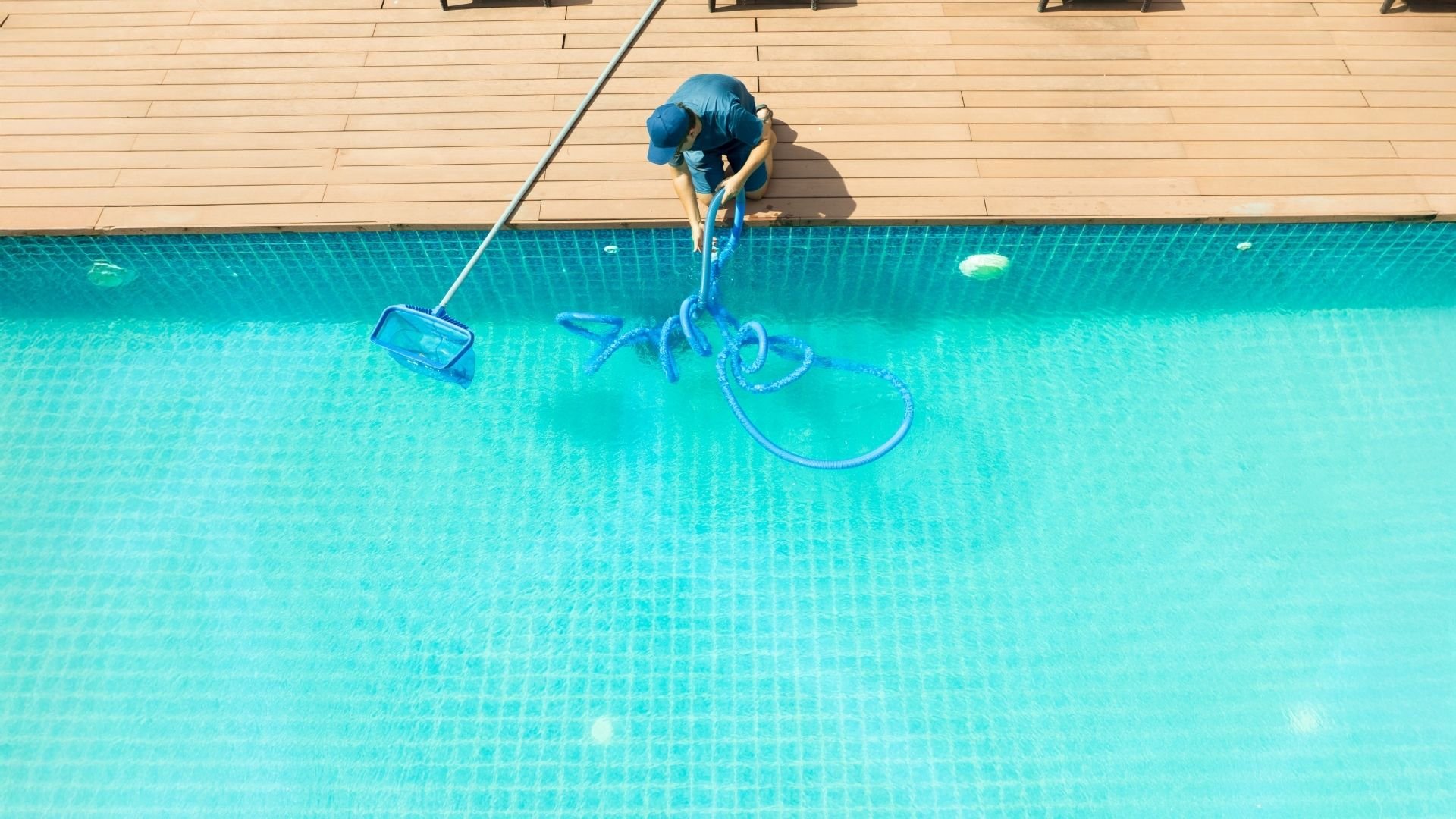 Person cleaning swimming pool with blue equipment and net from poolside