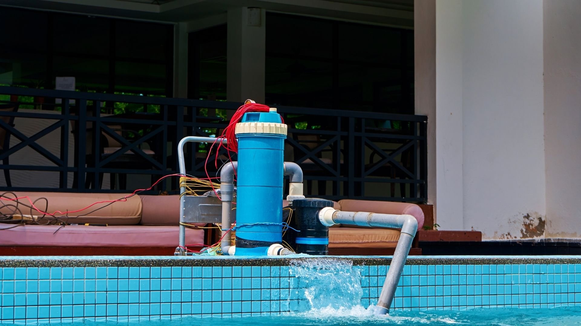 Blue pool filtration system with pipes and equipment beside tiled swimming pool