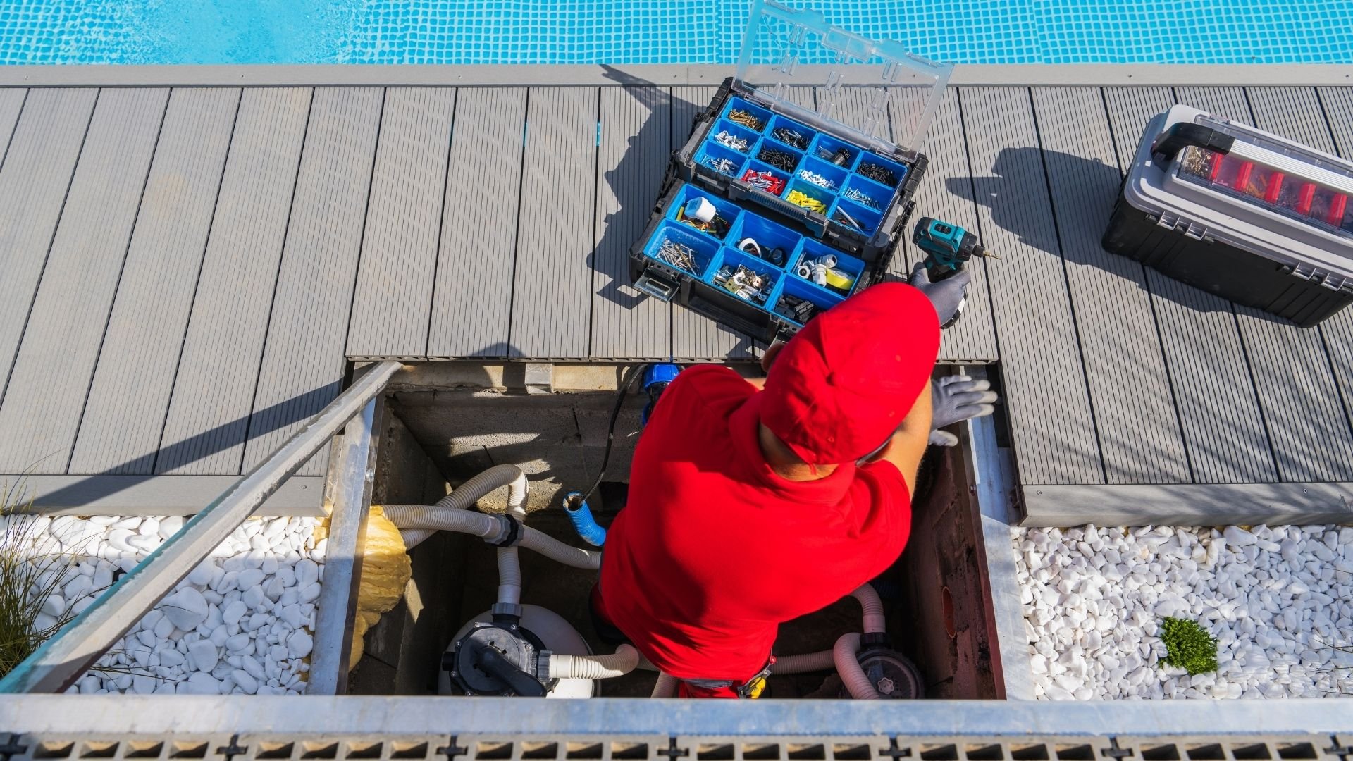 Overhead view of worker in red jacket maintaining pool equipment and toolbox on wooden deck