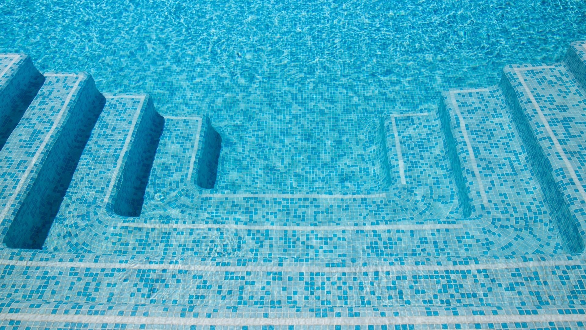 Underwater view of empty swimming pool with blue tile steps and clear water.