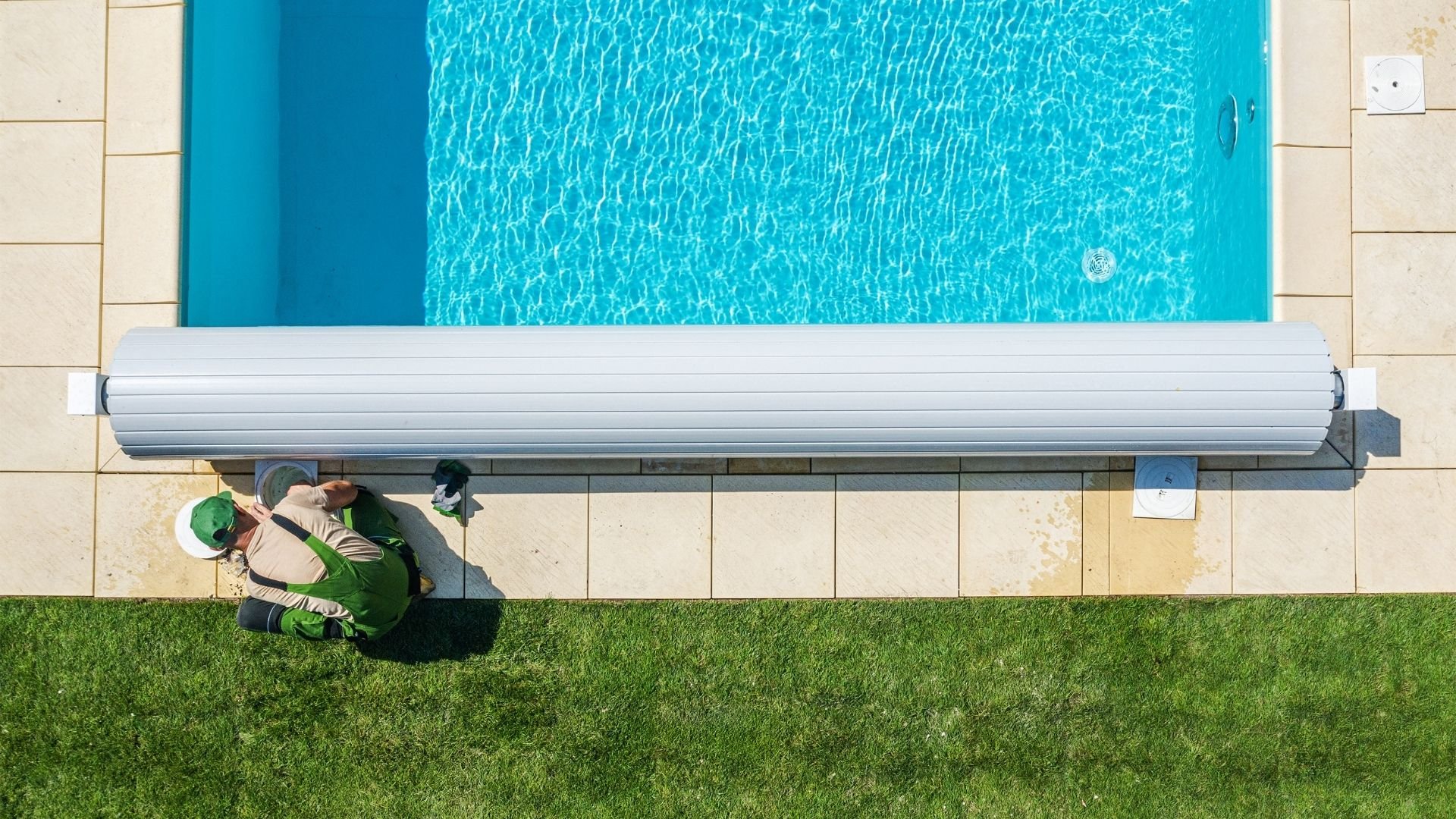 Aerial view of man working near turquoise swimming pool with rolled cover