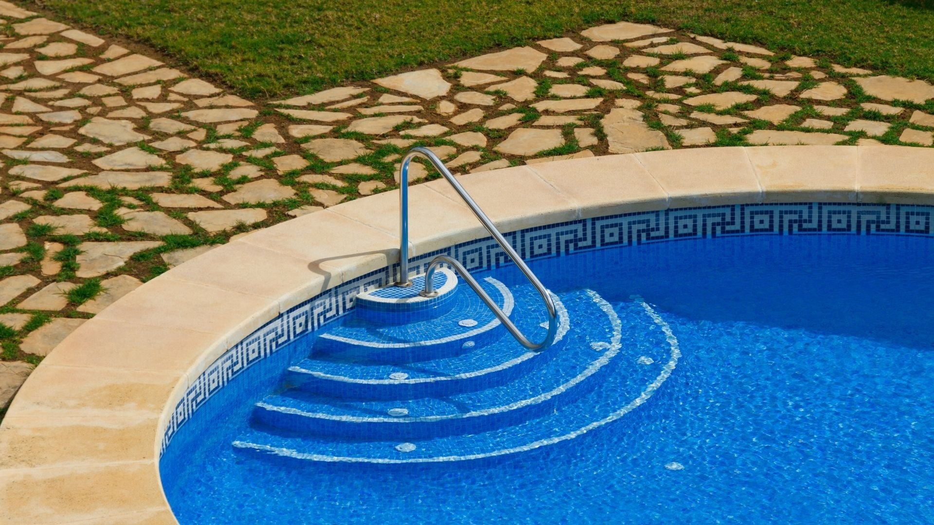 Swimming pool with metal ladder and stone patio walkway with green moss
