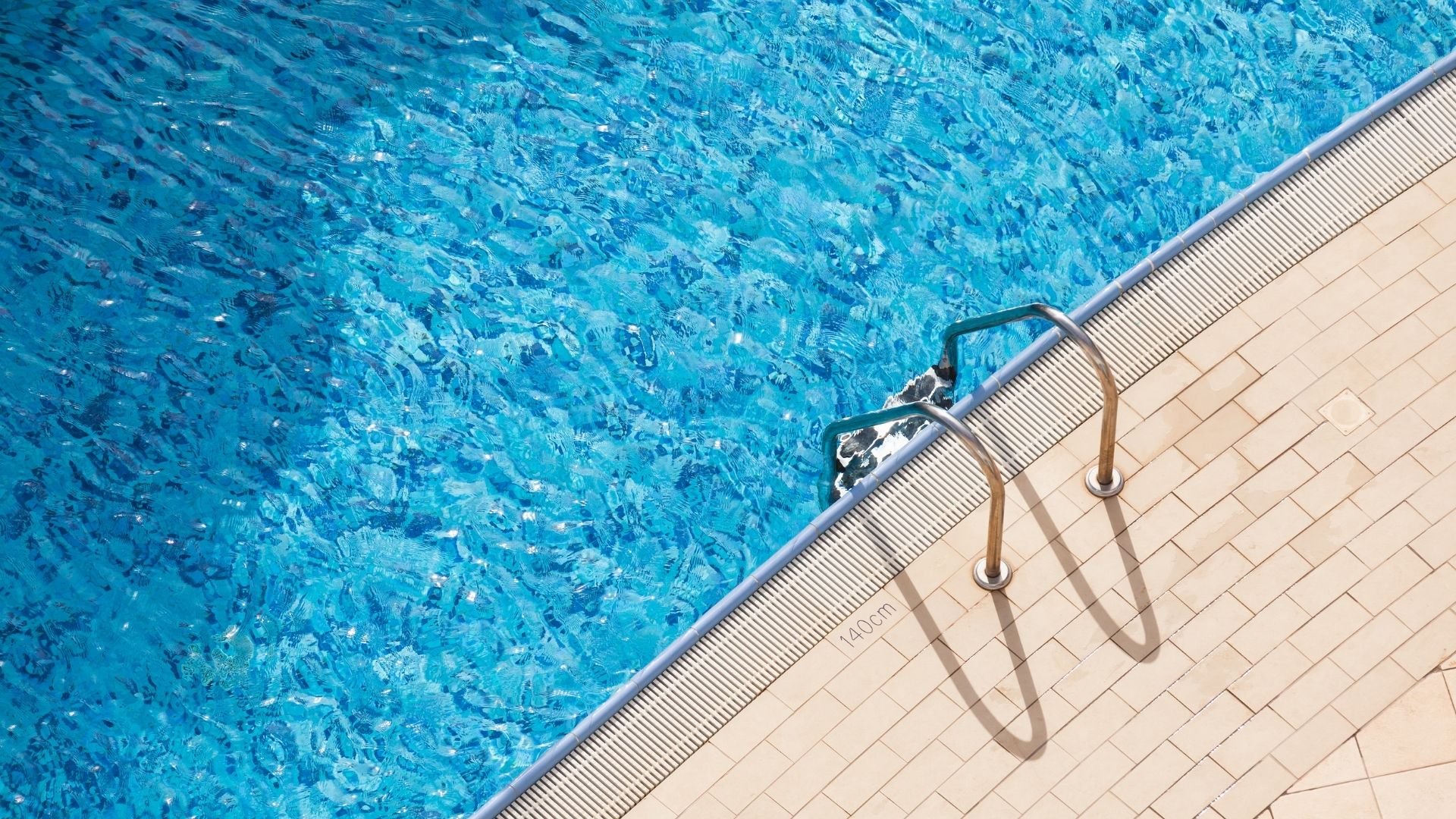 Swimming pool edge with metal handrail and clear blue water view